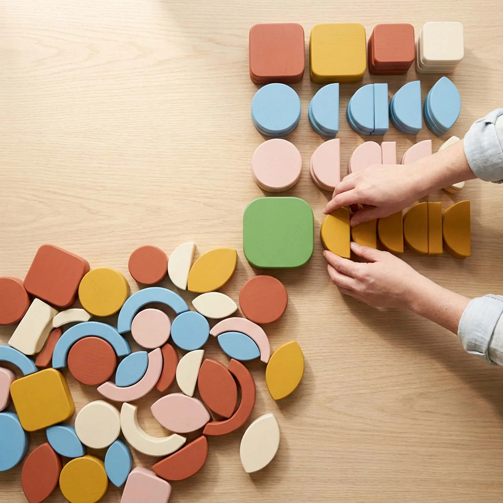 A jumble of colourful wooden shapes being sorted into tidy rows on a sunlit table, with a single green block where the mess becomes order.